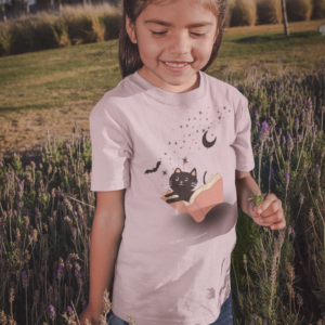 girl outside wearing a pink shirt with a cat and bat flying out of a book