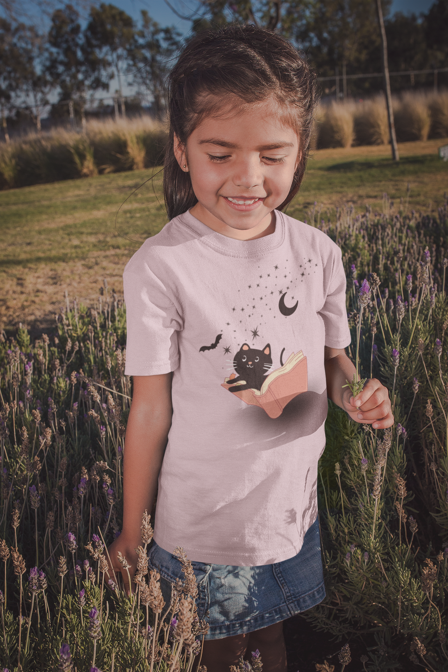girl outside wearing a pink shirt with a cat and bat flying out of a book