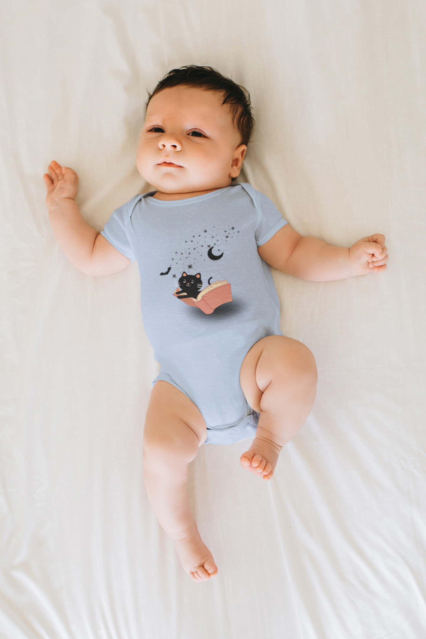 baby wearing a light blue onesie that has a cat and bat flying out of a book with stars and a moon cute halloween onesie