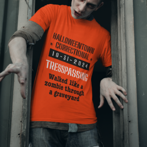 man dressed like a zombie wearing a shirt that says halloweentown correctional tresspassing walked like a zombie through a graveyard
