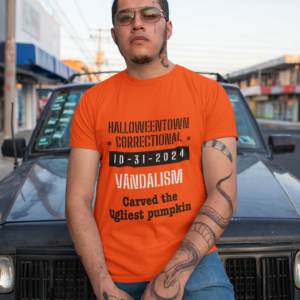 man wearing a shirt that says halloweentown correctional vandalism carved the uglist pumpkin