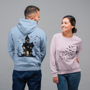 man and woman showing off back and front of shirts with flying bats on front and haunted house on the back