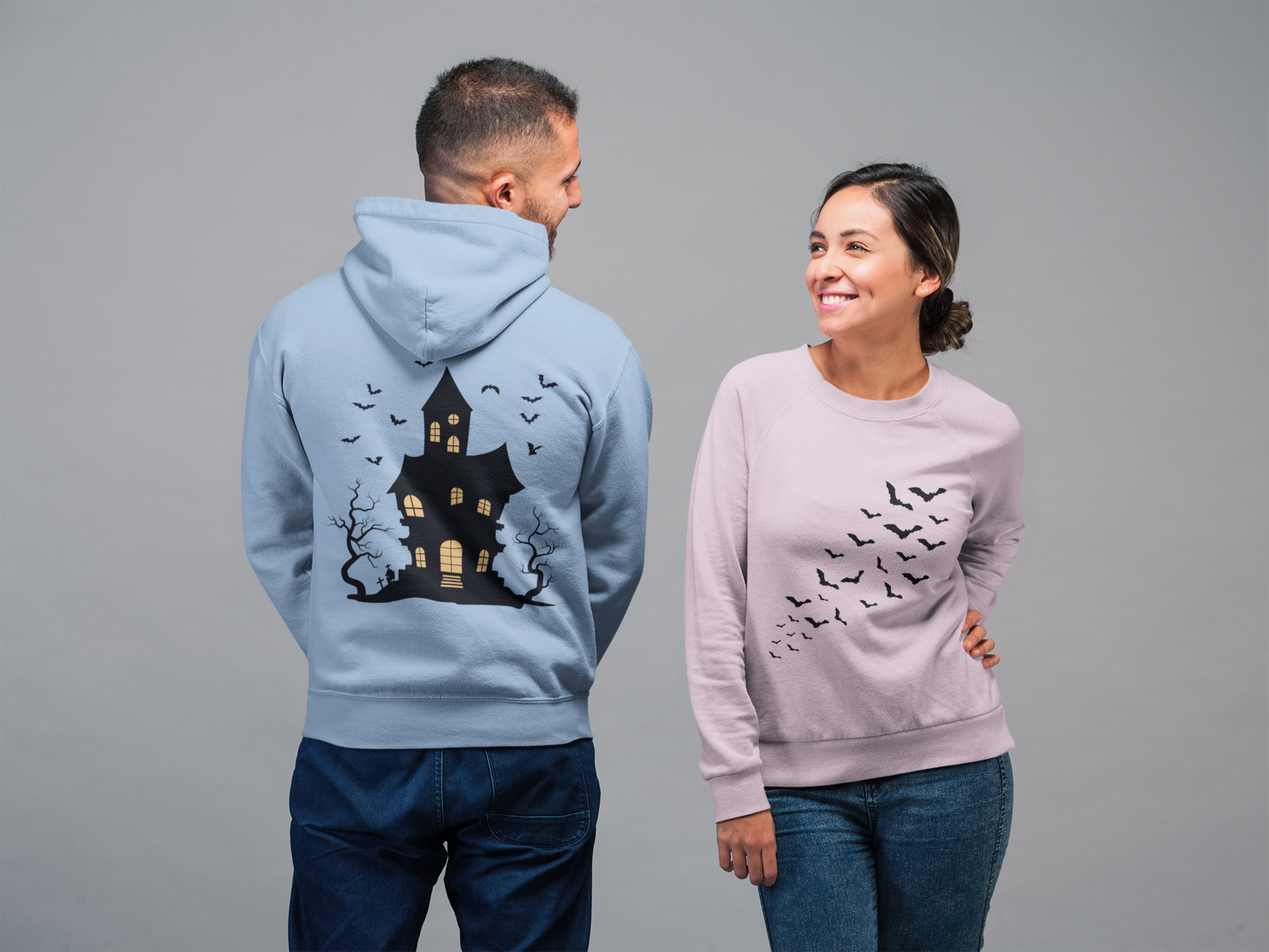 man and woman showing off back and front of shirts with flying bats on front and haunted house on the back