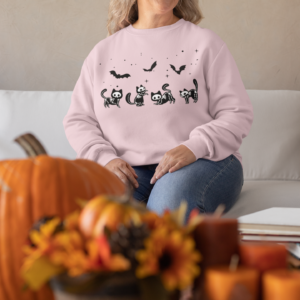 woman wearing a light pink halloween sweatshirt with skeleton kitties and bats